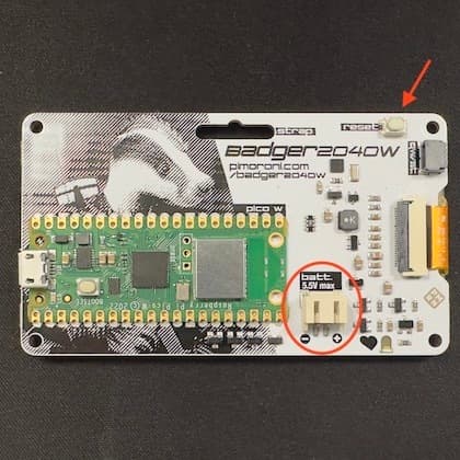 Back of the badge showing the reset button (arrow) and the connector for the batteries (circled)